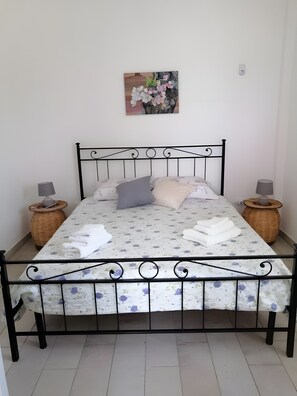 A bed with a metal frame, two nightstands with lamps, a woven basket, and a floral painting on the wall. - Villa 'Mios' with Private Terrace, Wi-Fi and Air Conditioning (Muro Leccese)