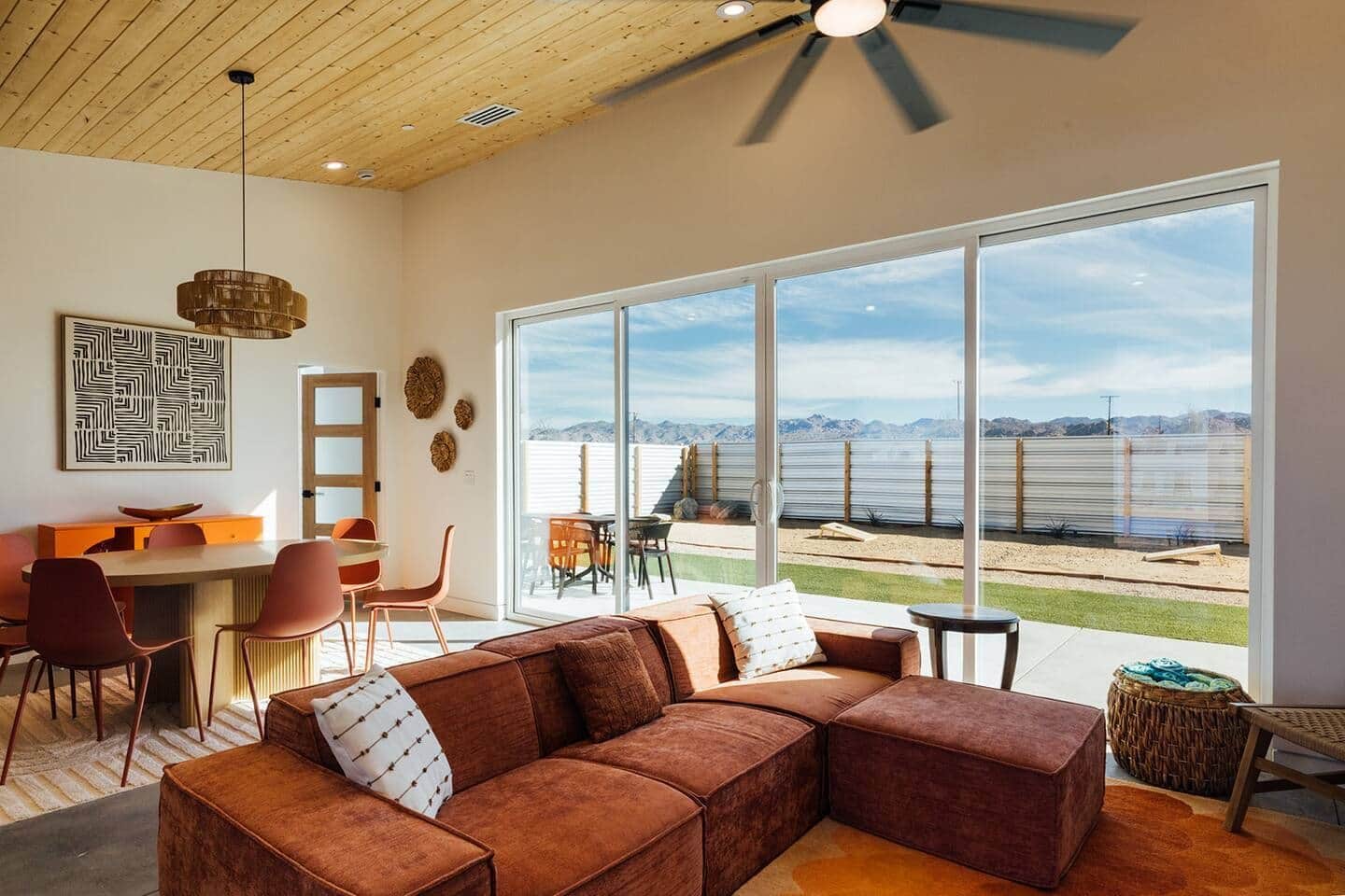 A modern living room with a large window, a sectional sofa, a dining area, and a ceiling fan.