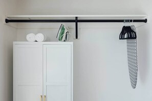 Ein weißer Kleiderschrank mit einer schwarzen, horizontalen Stange, auf der eine weiße Tasche und ein grün-weiß gemustertes Kleidungsstück liegen.