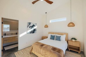 Ein modernes Schlafzimmer mit Bett, Nachttischen, einer Pendelleuchte, einem Gemälde und einem Fenster.
