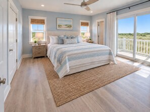 A bedroom with a large bed, a ceiling fan, and a view of the outdoors through a sliding door. - Direct Oceanfront-New Construction for 2027 (Kitty Hawk)