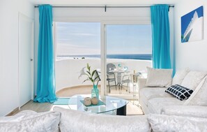 A room with a glass table, a white sofa, and a view of the beach. - Charming Apartment in Mijas (Mijas)