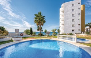 A swimming pool with a view of the sea, surrounded by palm trees and a white building with balconies. - Charming Apartment in Mijas (Mijas)
