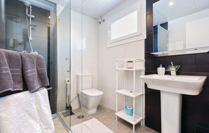 A modern bathroom with a glass shower enclosure, a white toilet, a white sink with a mirror above, and a towel rack with towels. - Charming Apartment in Mijas (Mijas)