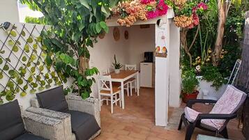 Un espacio de patio con una mesa y sillas, rodeado de plantas en macetas y un adorno de pájaro colgado en la pared.