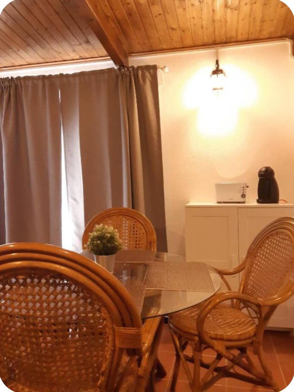Un'area pranzo con sedie in vimini, un tavolo in vetro, un armadietto bianco e un lampadario.