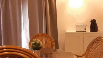 Un'area pranzo con sedie in vimini, un tavolo in vetro, un armadietto bianco e un lampadario.