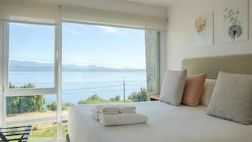 A bedroom with a large bed, a view of the sea, and artwork on the wall.