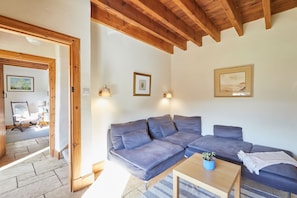 A living room with a sectional sofa, a coffee table, and two wall-mounted lamps. - Host Stay - West Loanend Cottage (Berwick-upon-Tweed)