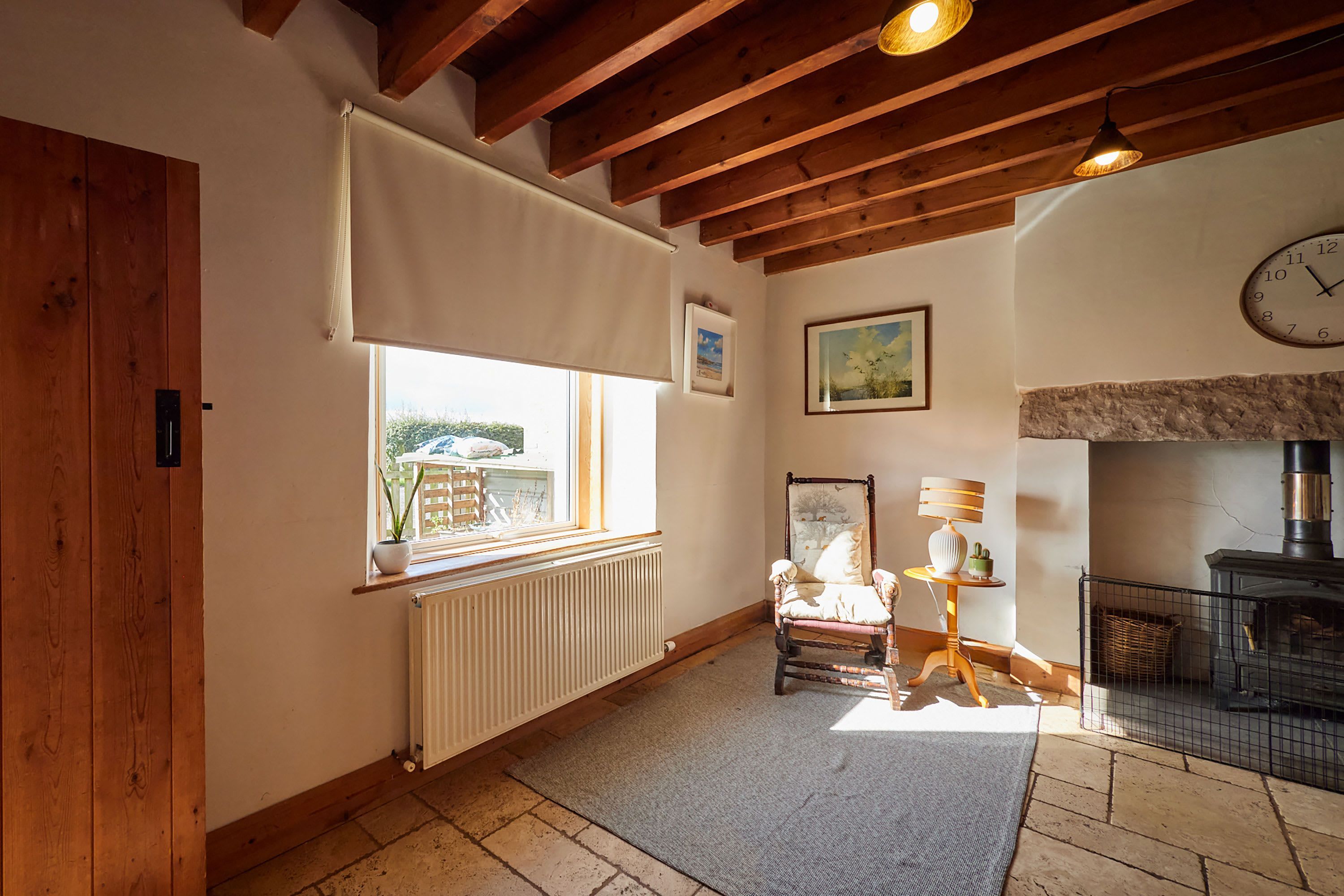 A cozy room with a wooden ceiling, a fireplace, a radiator, a chair, and a clock on the wall.