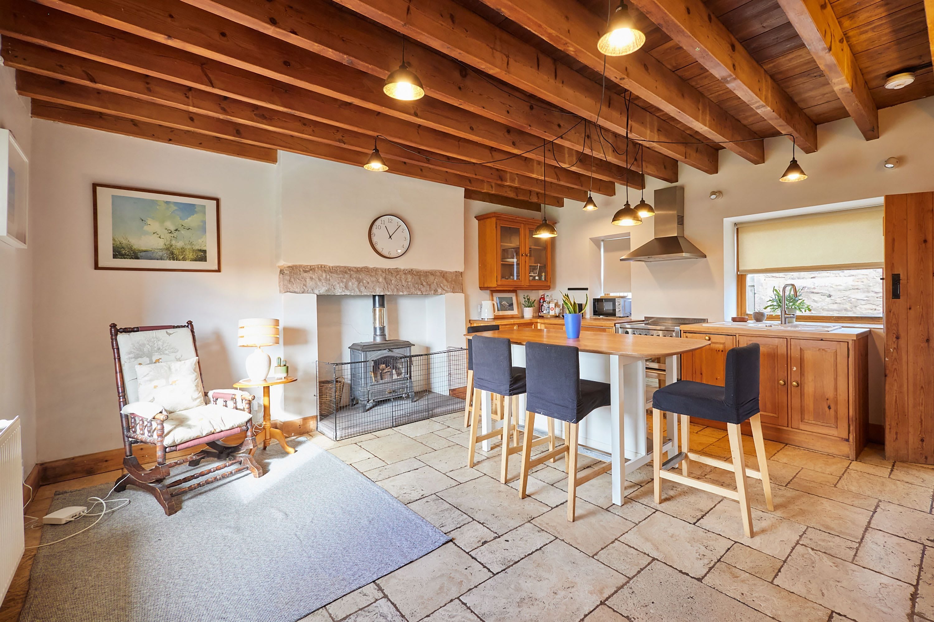 A kitchen with wooden beams, a stone fireplace, and a bar area with chairs.