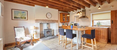 A kitchen with wooden beams, a stone fireplace, and a bar area with chairs.