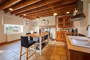 A kitchen with a wooden table, chairs, a sink, cabinets, and a window. - Host Stay - West Loanend Cottage (Berwick-upon-Tweed)