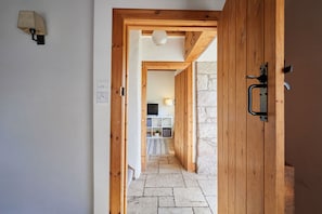 A wooden door leading to a stone-walled room with a television and a white shelf. - Host Stay - West Loanend Cottage (Berwick-upon-Tweed)