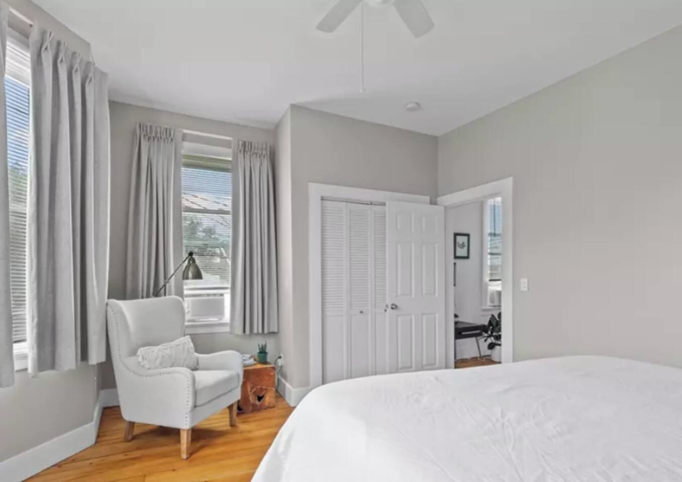 A bedroom with a large bed, a chair, a desk, and a window with curtains.