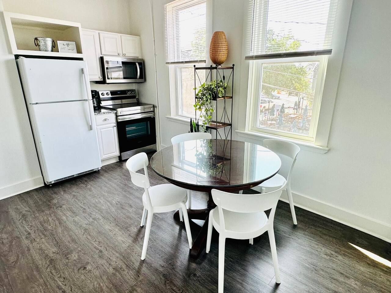A modern kitchen with white cabinets, a refrigerator, an oven, a microwave, and a dining table with chairs.