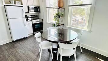 A modern kitchen with white cabinets, a refrigerator, an oven, a microwave, and a dining table with chairs.