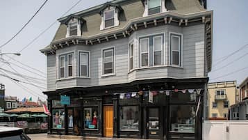 A two-story building with a bay window on the second floor, a storefront with mannequins, and a flag on the corner.