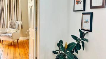 A hallway with wooden flooring, a potted plant, and framed artwork on the wall.