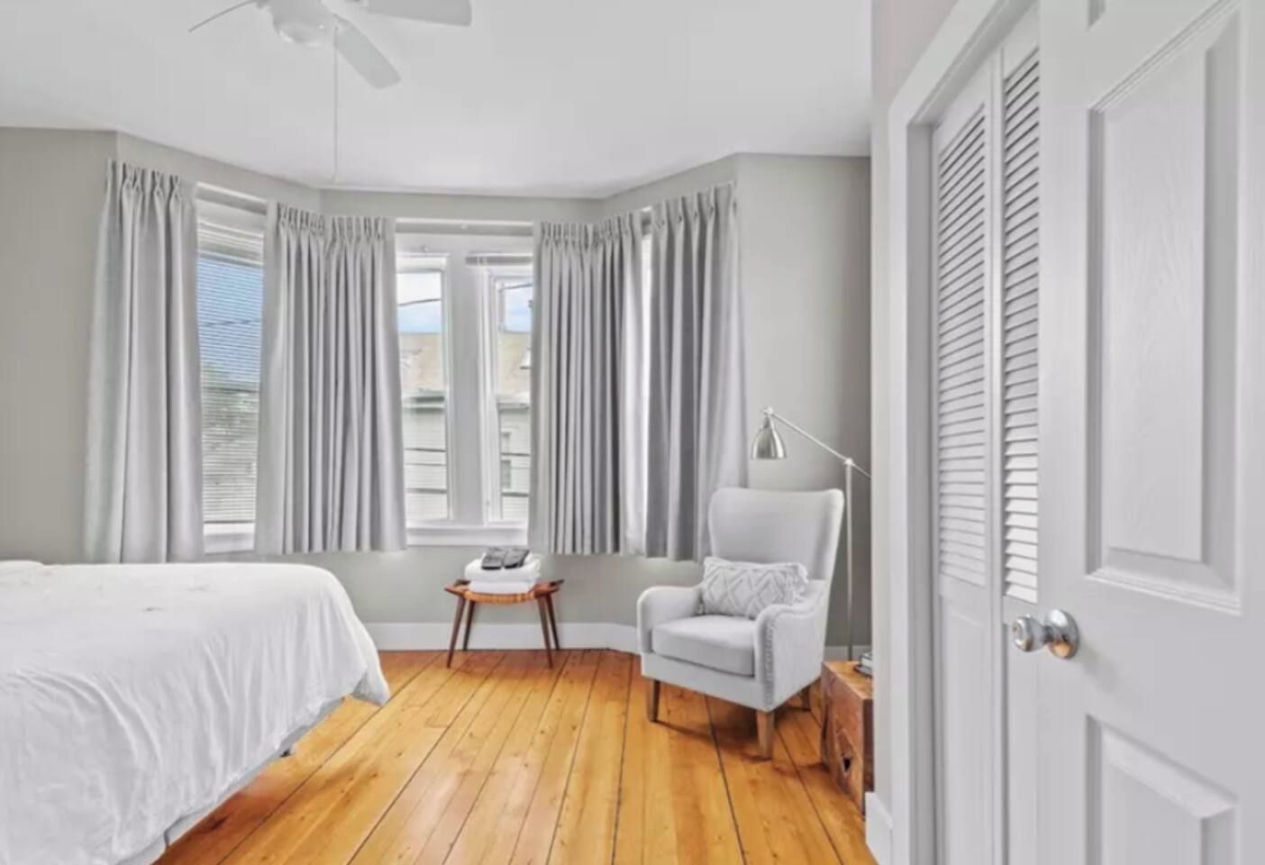 A bedroom with a bed, a chair, a small table, and a window with curtains.