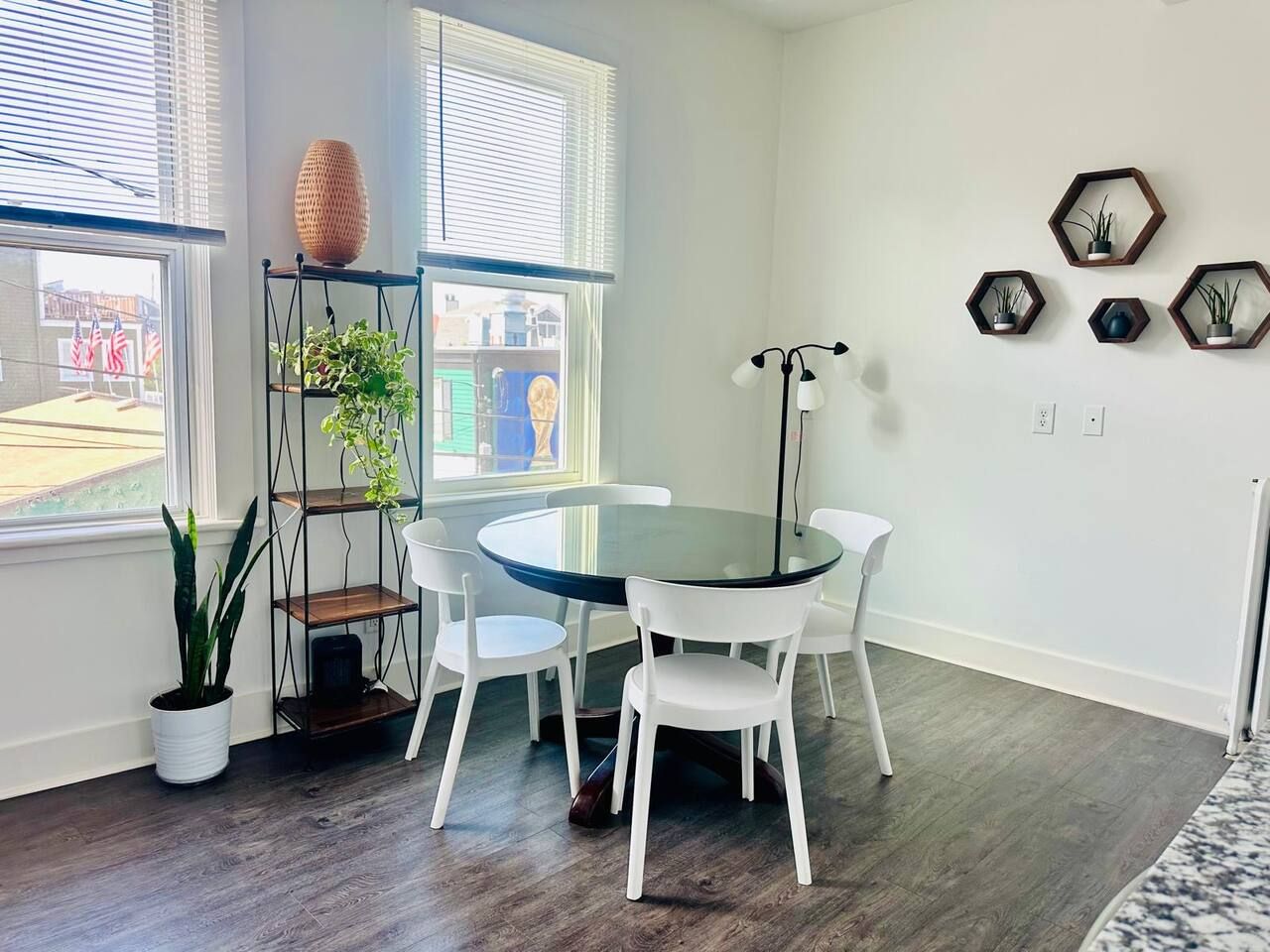 A dining area with a round glass table and white chairs, a potted plant, and a floor lamp.