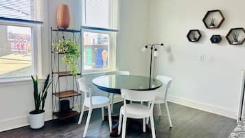 A dining area with a round glass table and white chairs, a potted plant, and a floor lamp.