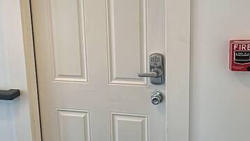 Une porte blanche dotée d’un clavier pour l’ouverture et d’un détecteur d’incendie fixé au mur.
