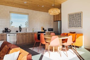 A modern kitchen with a dining area, wooden ceiling, and a large window. - Midnight Sun | Custom pool, pickleball court, spa (Joshua Tree)