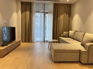 A modern living room with a sectional sofa, a flat-screen TV on a wooden stand, and a small round table. - Marina Village: luxury 1-bedroom apartment by seaside in Nardaran, Baku (Nardaran)