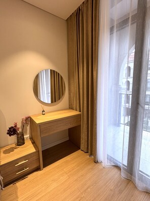 A room with a wooden desk, a round mirror, a vase with flowers, and a view through sheer curtains. - Marina Village: luxury 1-bedroom apartment by seaside in Nardaran, Baku (Nardaran)