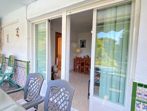 A room with a sliding glass door leading to an outdoor area, a dining table with chairs, and a small table with a lamp. - Apartment in Nerja Near Burriana Beach (Nerja)