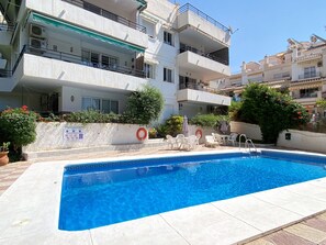 A swimming pool with a tiled edge, surrounded by outdoor seating and a white building with multiple balconies. - Apartment in Nerja Near Burriana Beach (Nerja)