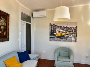 Ein Wohnzimmer mit einer Couch, einem Sessel, einem Gemälde eines Straßenbahns und einer Deckenleuchte.