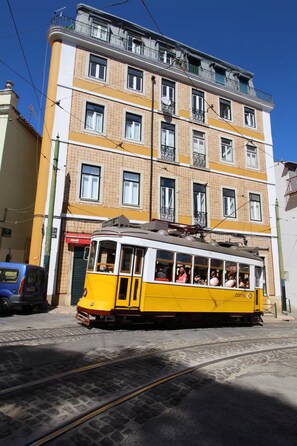 Eine gelbe Straßenbahn mit Fahrgästen fährt an einem mehrstöckigen Gebäude mit Balkonen und verzierten Fenstern vorbei.