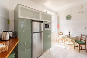 Eine kompakte Küche mit integriertem Mikrowellenherd, einem Edelstahl-Kühlschrank und einem Essbereich mit Tisch und Stühlen.