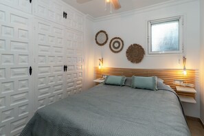 A bedroom with a bed, a nightstand, a window, and a wall with decorative items. - Apartment in Nerja Near Burriana Beach (Nerja)