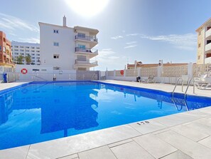 A swimming pool with a clear blue water surface, surrounded by a white tiled deck and a white fence. - Apartment in Nerja Near Burriana Beach (Nerja)