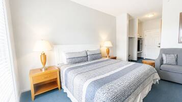 A bedroom with a bed, two bedside tables with lamps, a grey sofa, and a door leading to a bathroom.