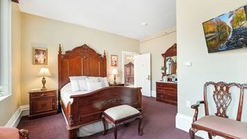 A bedroom with a large wooden bed, bedside tables, a chair, and a painting on the wall.