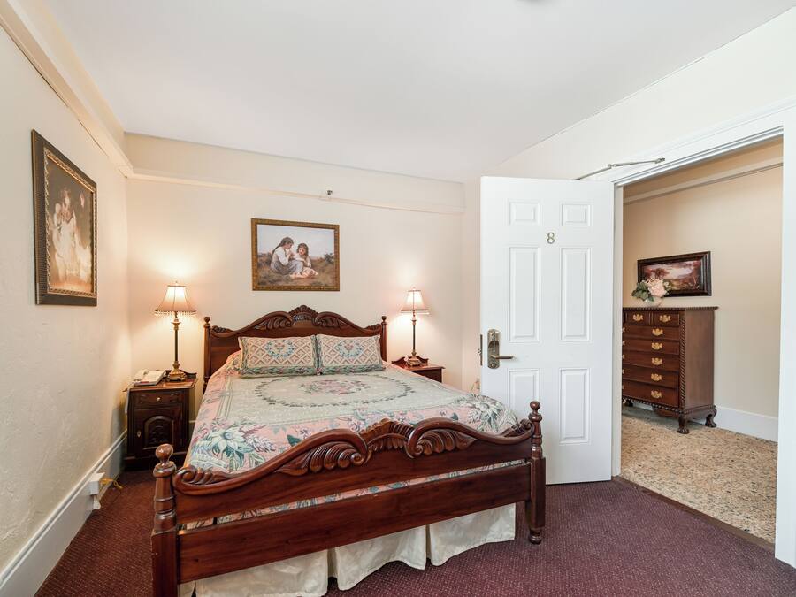 A bedroom with a wooden four-poster bed, two bedside lamps, a floral bedspread, and a door leading to another room.