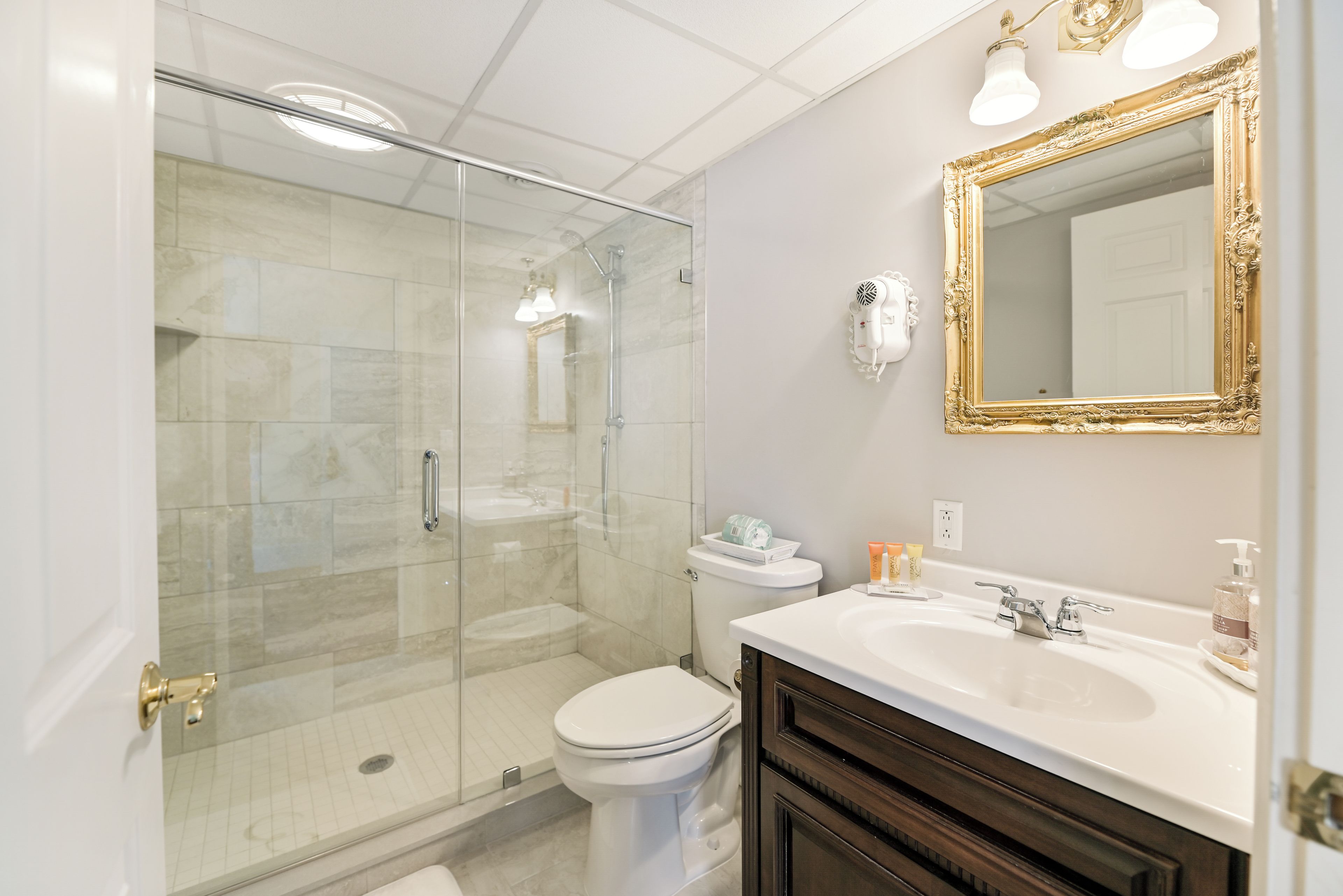 A bathroom with a glass-enclosed shower, a white toilet, a vanity with a mirror, and toiletries on the sink.