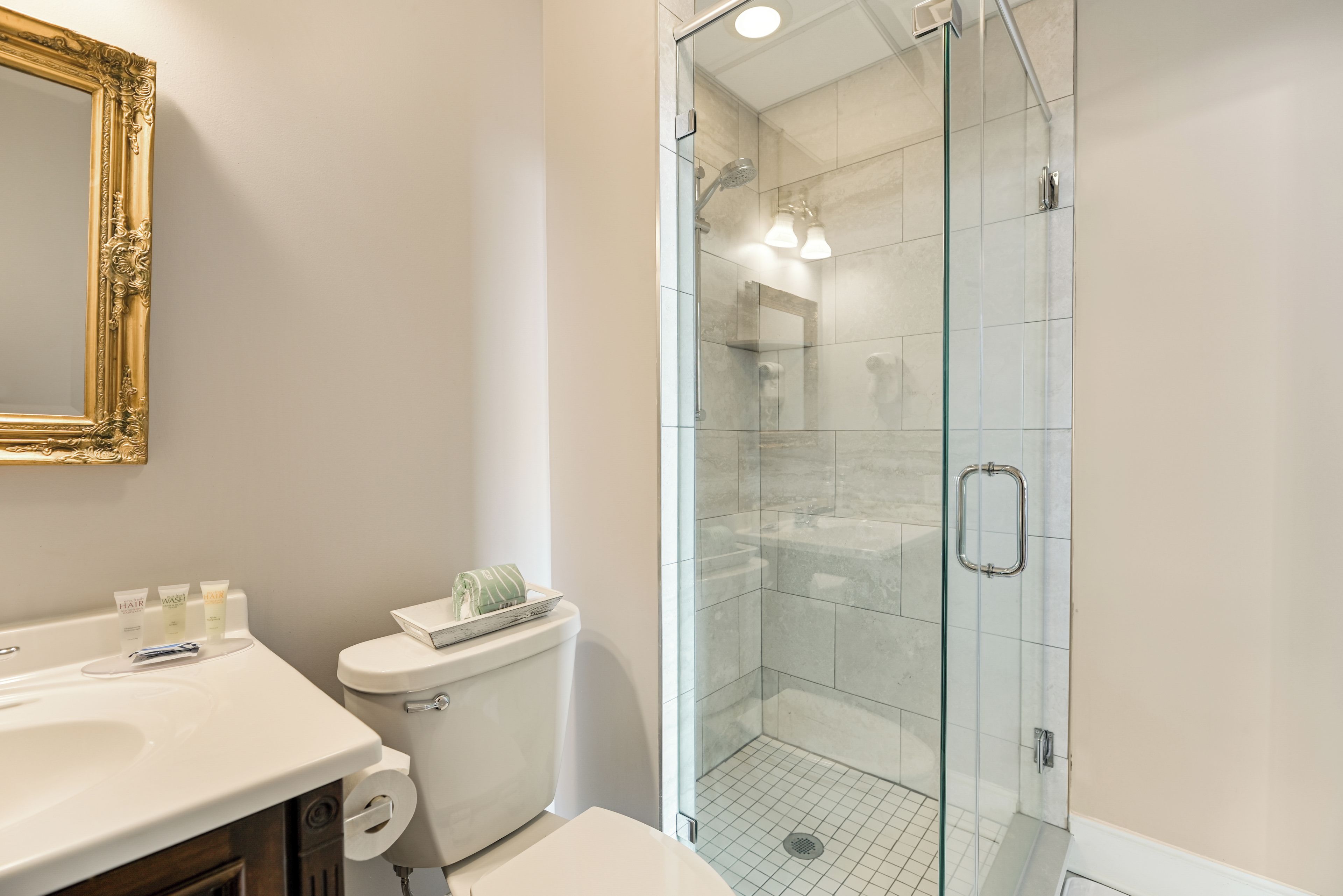 A bathroom with a glass shower enclosure, a toilet, and a sink with toiletries.