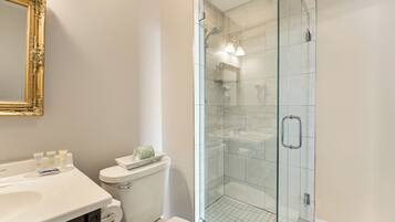 A bathroom with a glass shower enclosure, a toilet, and a sink with toiletries.