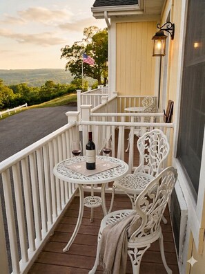 A balcony with white railings, a table with chairs, a bottle of wine, and a flag.