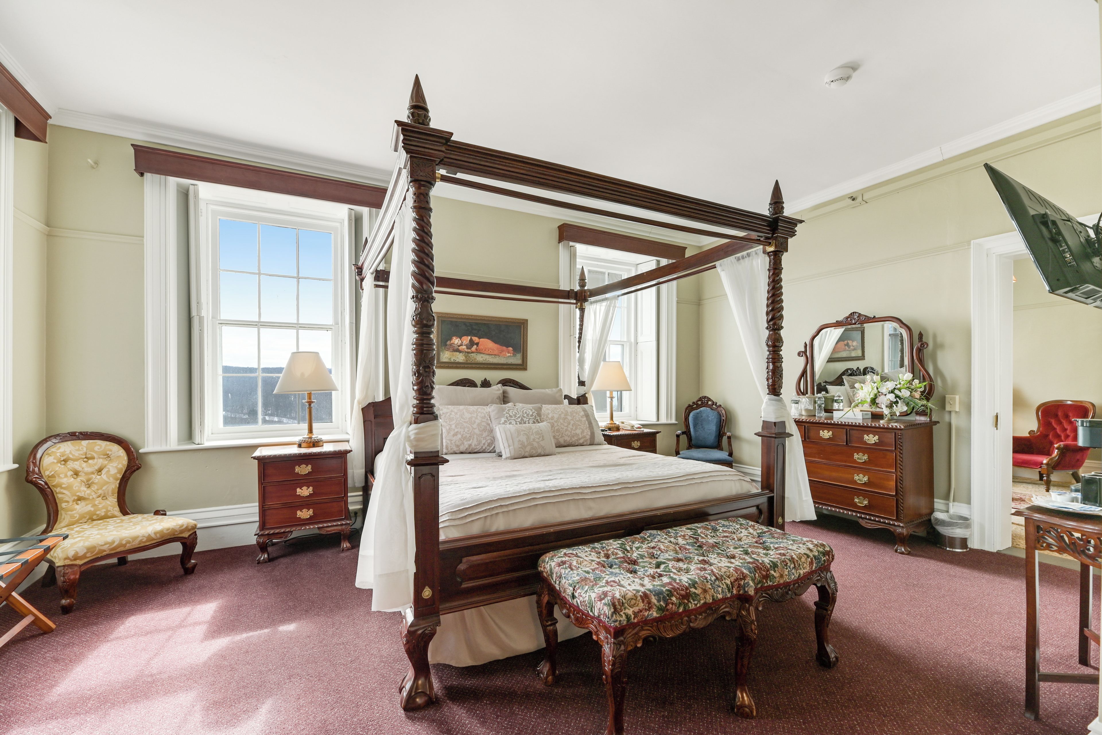 A traditional four-poster bed with a canopy, a sitting bench, and a wooden dresser with a mirror.