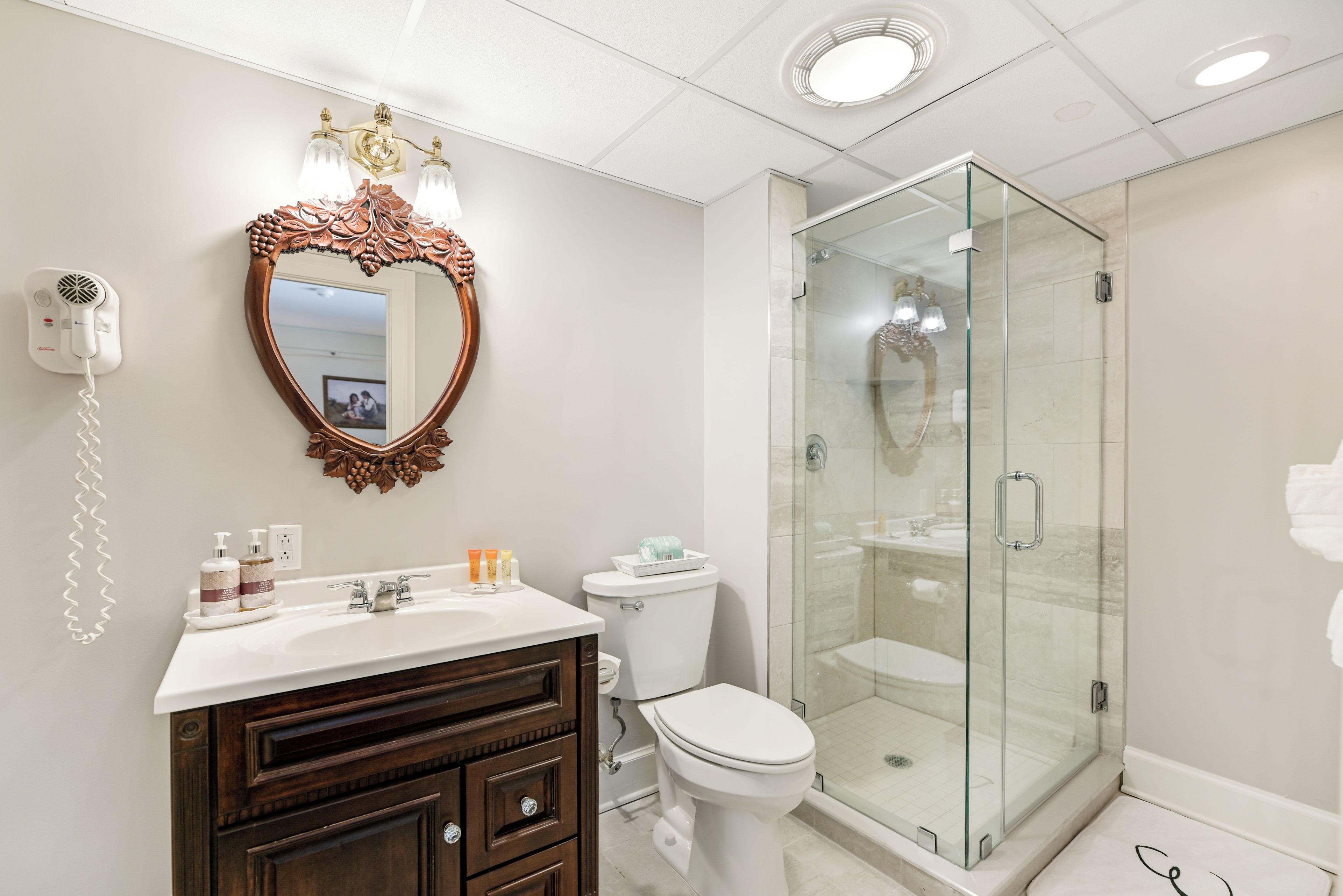 A bathroom with a vanity, a toilet, a shower enclosure, and a hairdryer mounted on the wall.