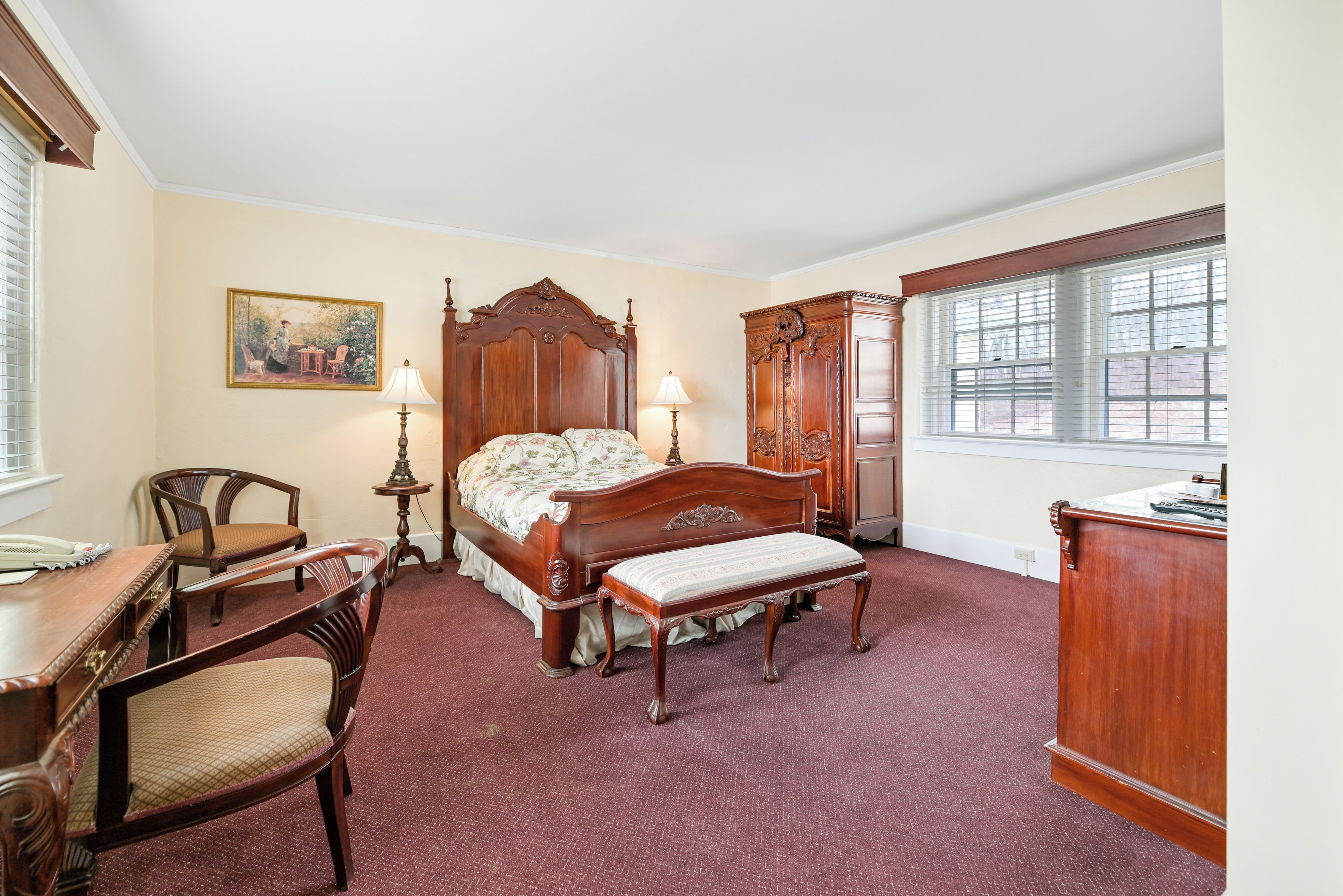 A bedroom with a four-poster bed, a desk, a chair, a dresser, and a window with blinds.