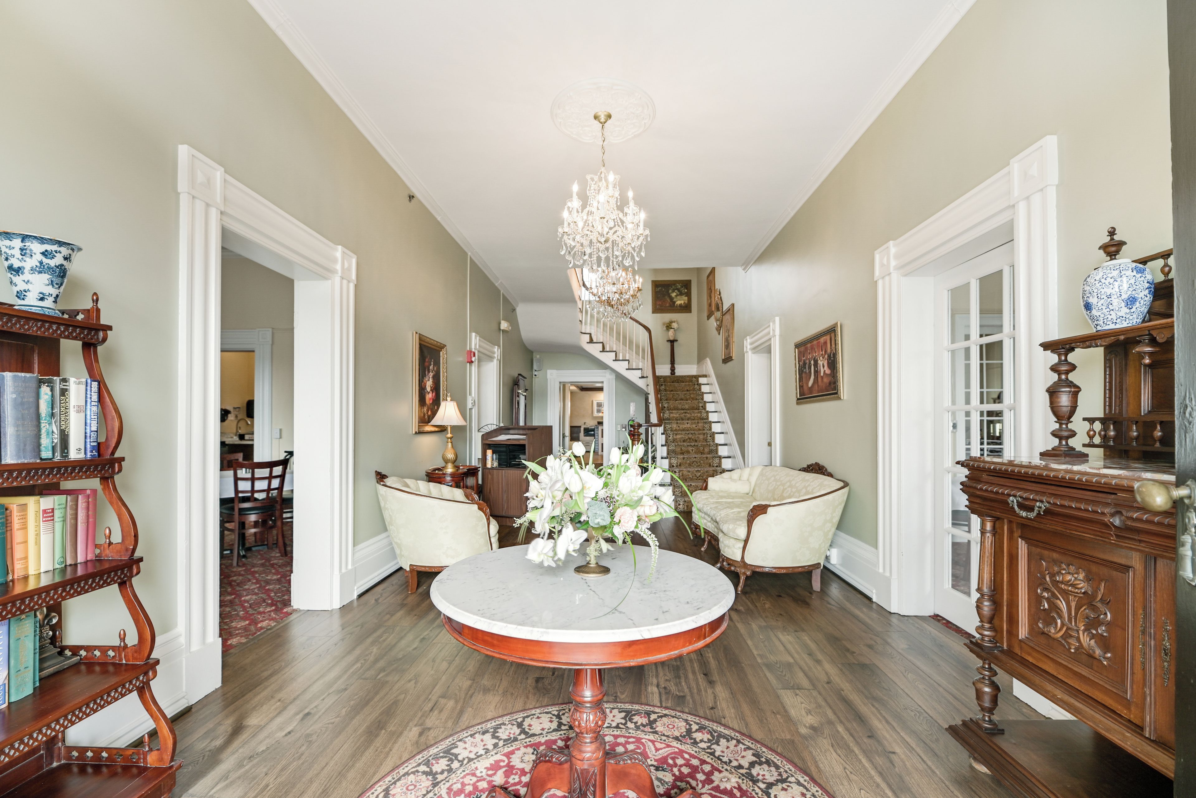 A spacious foyer with a grand chandelier, a round marble table, and a staircase leading to the upper floor.