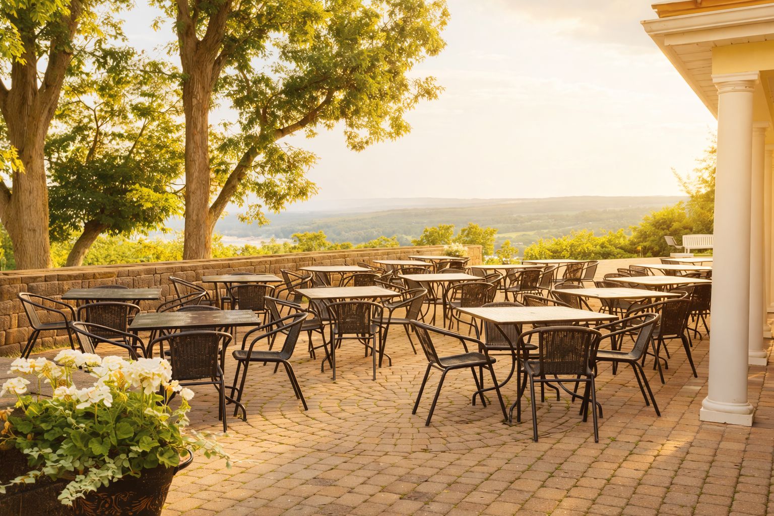 Un patio al aire libre con varias mesas y sillas, rodeado de árboles y vistas al paisaje.