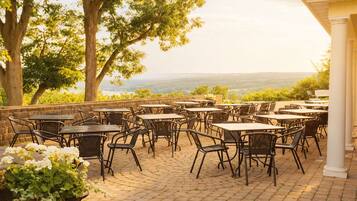 Un patio al aire libre con varias mesas y sillas, rodeado de árboles y vistas al paisaje.